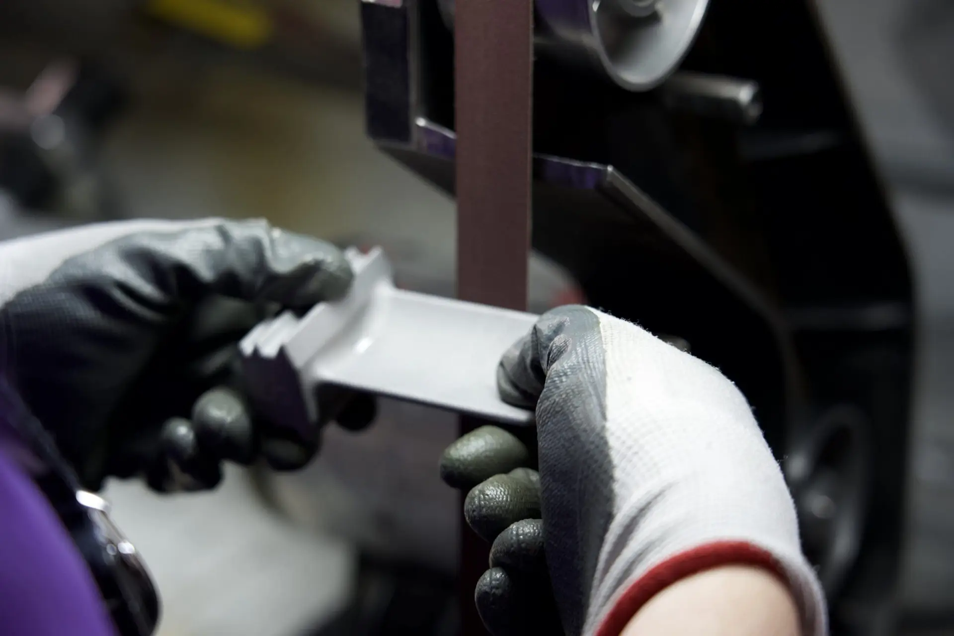 Technician using a belt sander to hand finish and deburr a metal component.